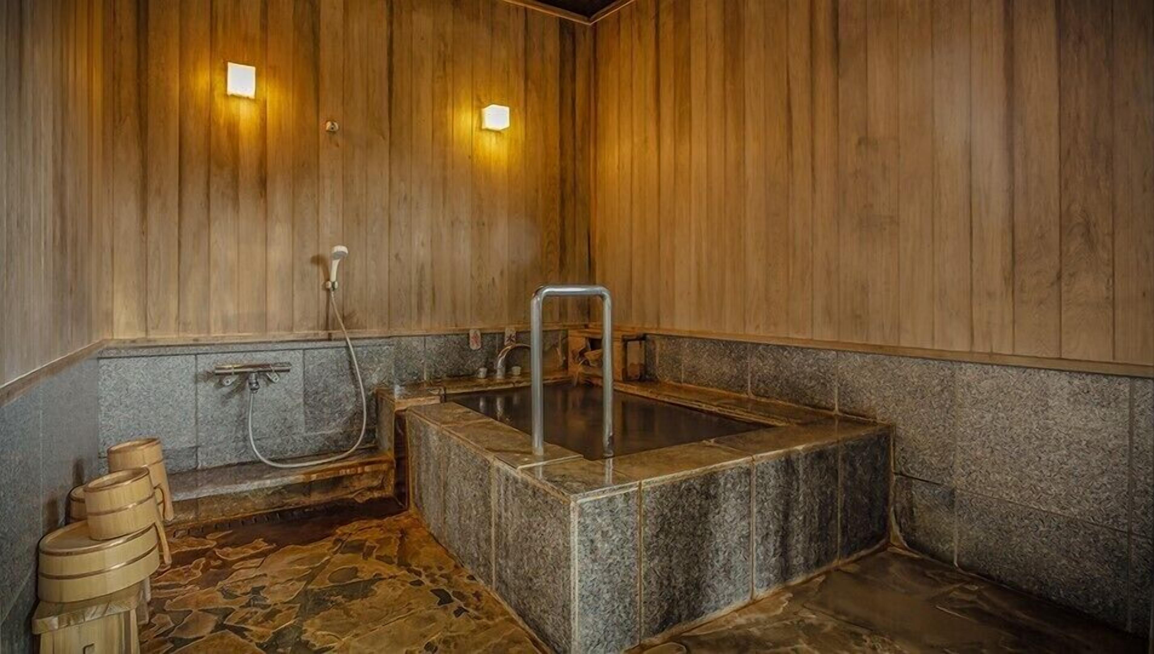 A wooden interior with a stone hot tub, a wooden bench, and a metal ladder.