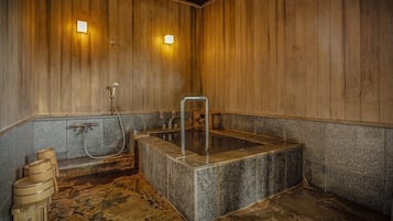 A wooden interior with a stone hot tub, a wooden bench, and a metal ladder.