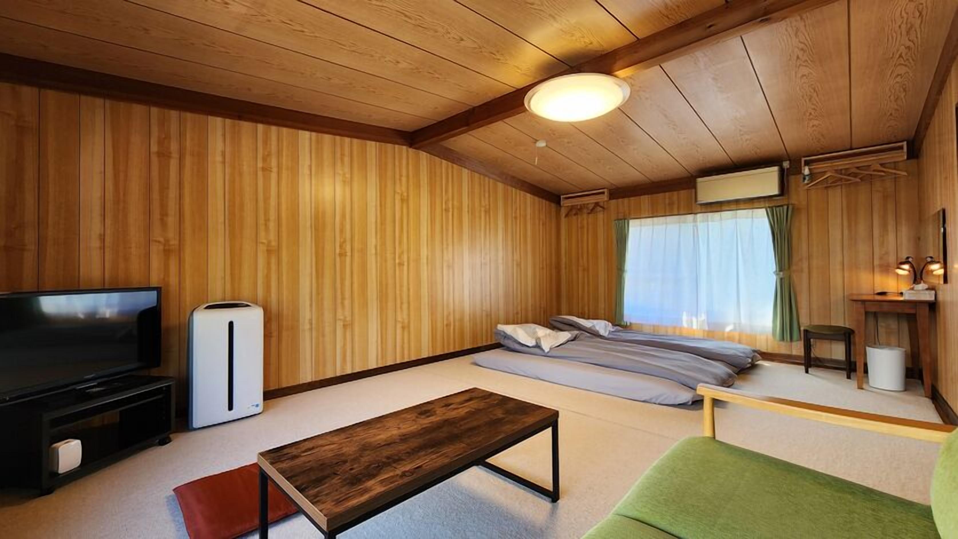 Una habitación con paneles de madera, un sofá, un televisor, una mesita y una cama.