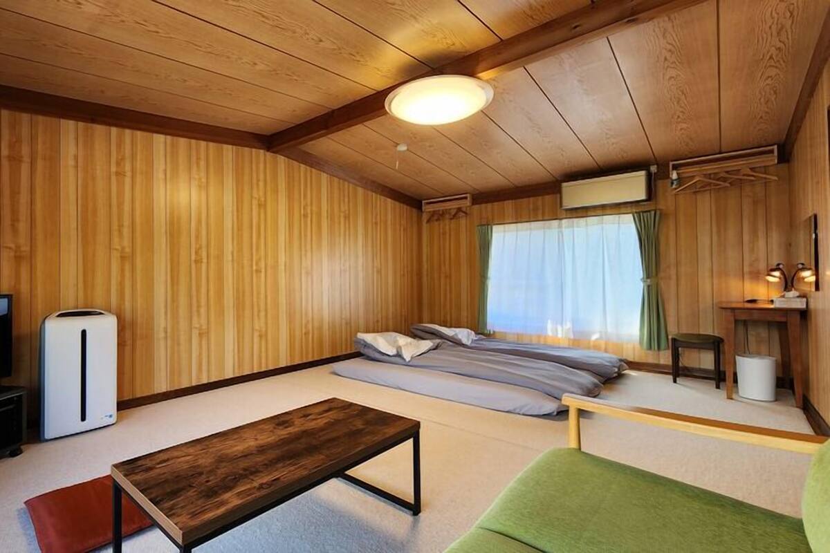 A wooden-paneled room with a sofa, a TV, a small table, and a bed.