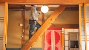 A person climbing a wooden staircase inside a traditional building with tatami flooring and sliding doors. - Minshuku Yaichi (Gujo)