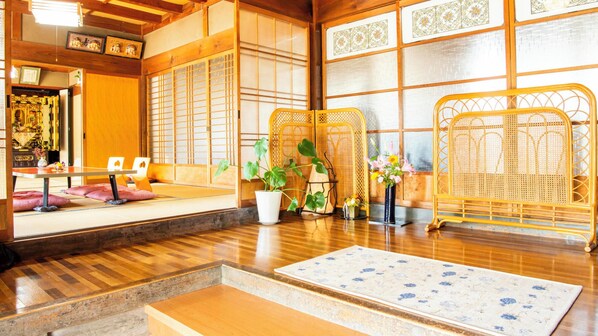 A traditional Japanese room with tatami flooring, a low table, cushions, a potted plant, and a woven screen.