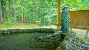 A stone water feature with a statue, surrounded by a wooden fence and trees. - Minshuku Yaichi (Gujo)