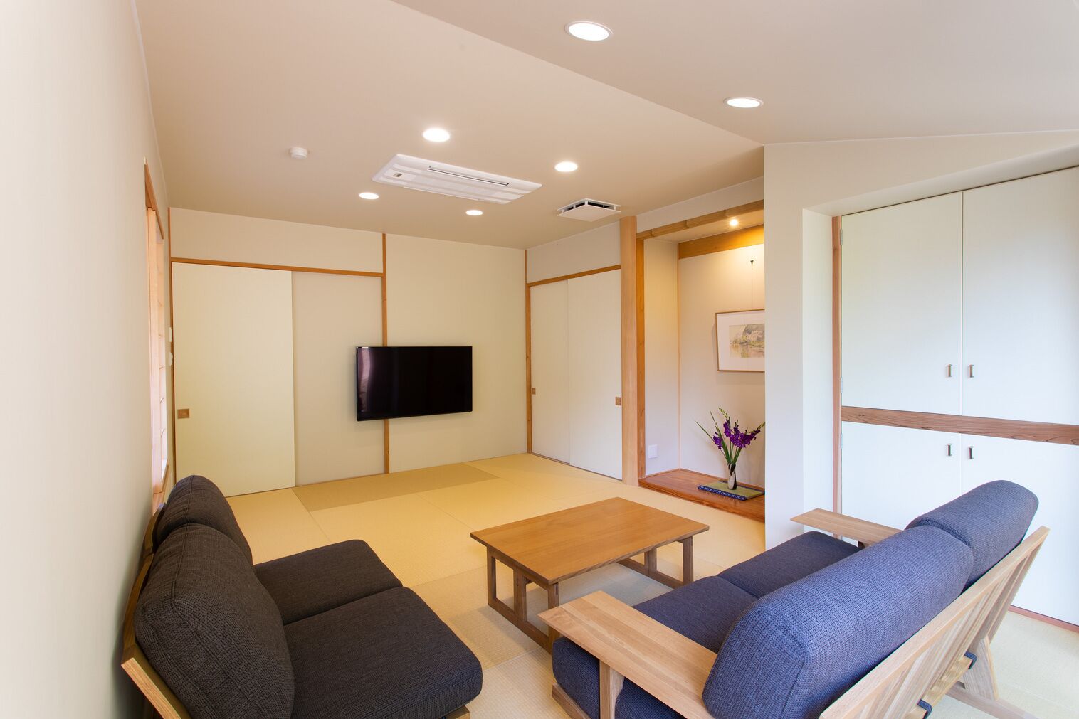 Un saló modern amb terra de tatami, un televisor de pantalla plana, una taula de centre de fusta i un sofà.