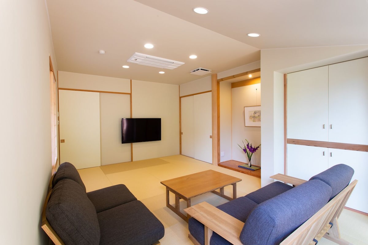 A modern living room with tatami flooring, a flat-screen TV, a wooden coffee table, and a sofa.