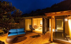Un'area relax esterna moderna con un terrazzo in legno, un divano blu e uno spazio vetrato con camino.