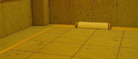 A room with a tiled floor, wooden walls, and a single roll of paper on the floor.