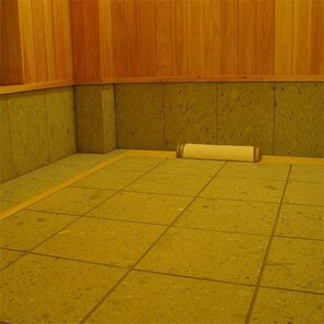 A room with a tiled floor, wooden walls, and a single roll of paper on the floor. - Kamai Onsen Ippenan (Kyotango)