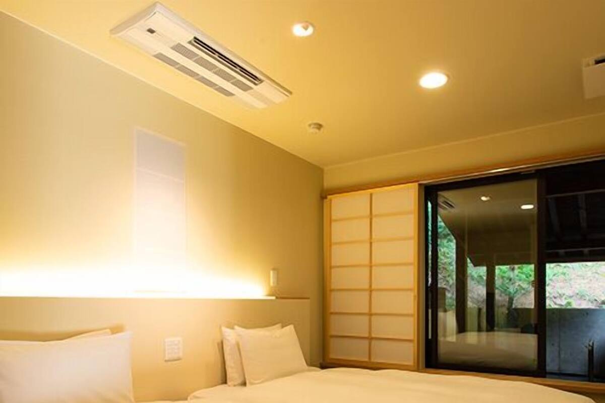 A hotel room with a large bed, an air conditioning unit, a sliding door with a view, and a wall-mounted light.