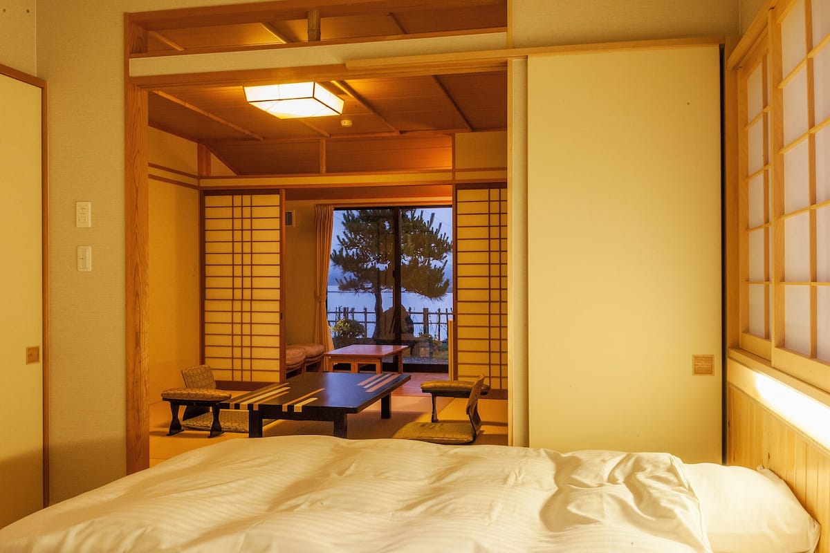 A traditional Japanese room with tatami flooring, a low table, a bench, and a bed.