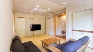 A modern living room with a flat-screen TV, two sofas, a wooden coffee table, and a cabinet with sliding doors. - Kamai Onsen Ippenan (Kyotango)