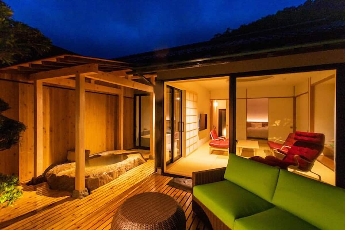 A modern outdoor living area with a wooden deck, a hot tub, and a green sofa.