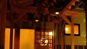 A traditional Japanese building entrance with wooden beams, a sliding door with glass panels, and a small outdoor area with a bench. - Kamai Onsen Ippenan (Kyotango)