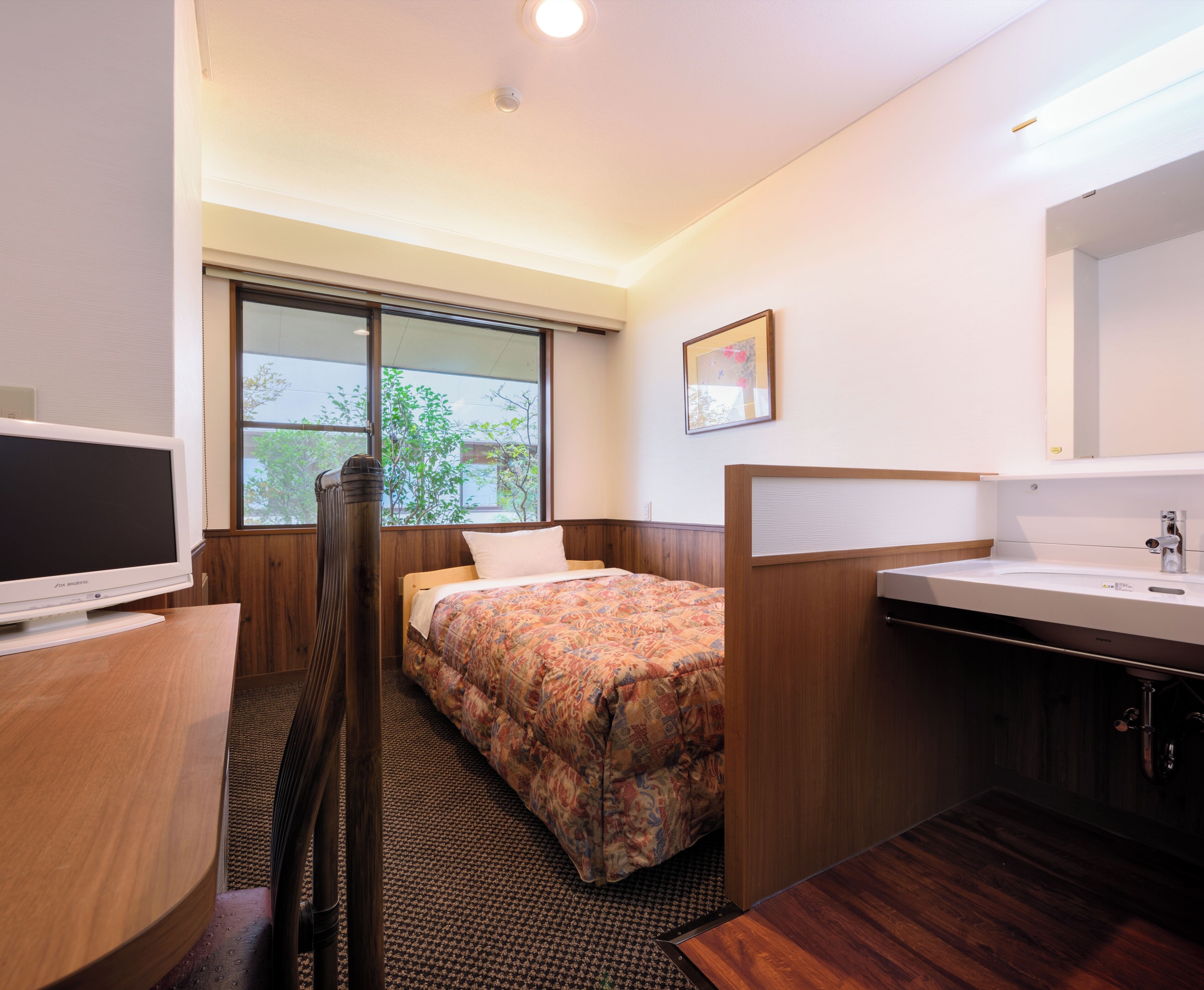 Habitación de hotel con cama, televisión, ventana, baño con lavamanos y espejo.