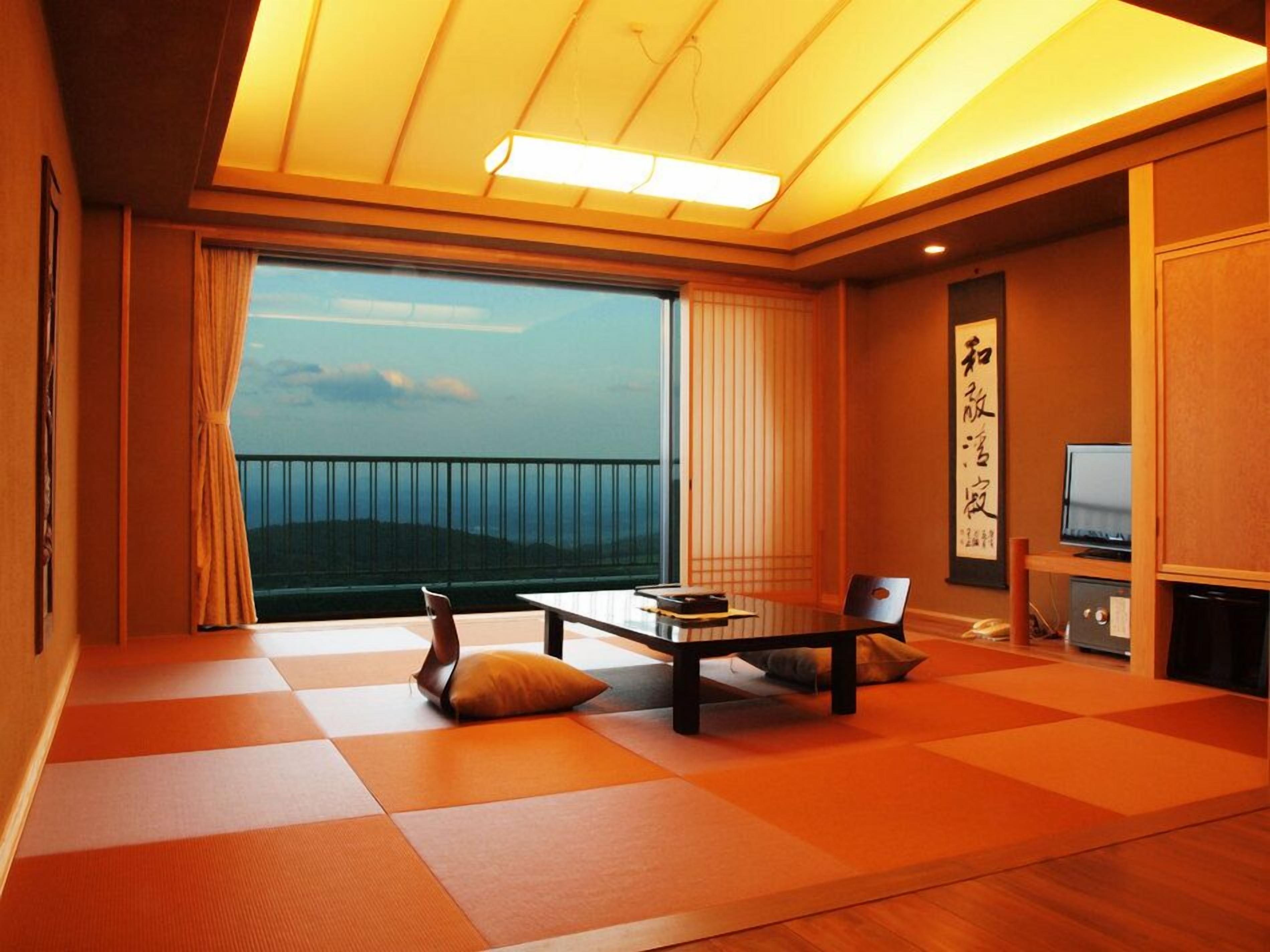 Una habitación con esteras de tatami, una mesa baja, una silla, un televisor y un ventanal con vistas.
