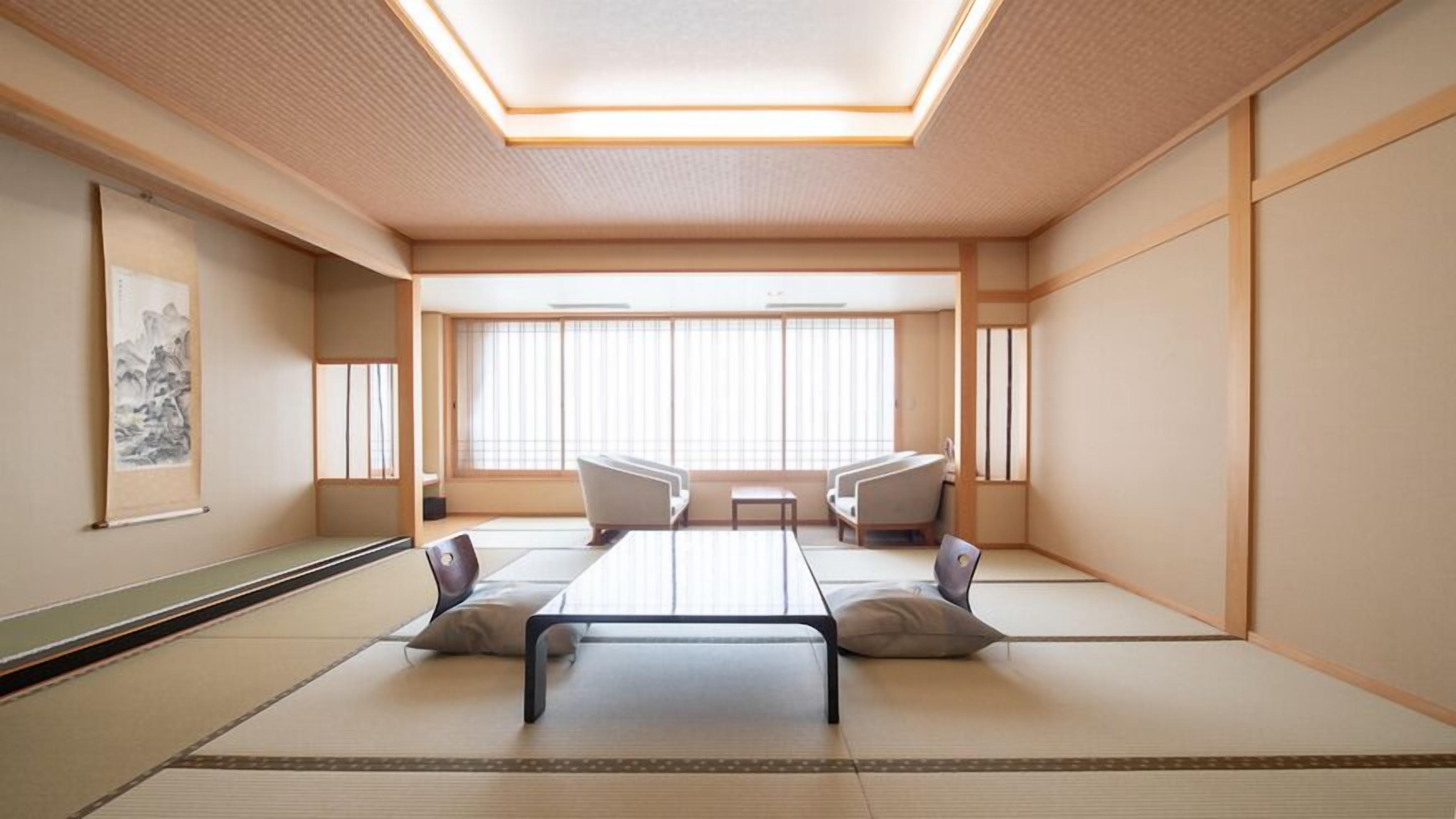 Una habitación con tatami, una mesa baja, dos sillas y un ventanal con persianas verticales.