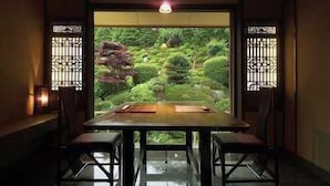 A dining area with a table and chairs, a view of a garden through a window with decorative grilles, and a hanging light fixture. - Dake Onsen Nagame no Yakata Kounkaku (Nihommatsu)