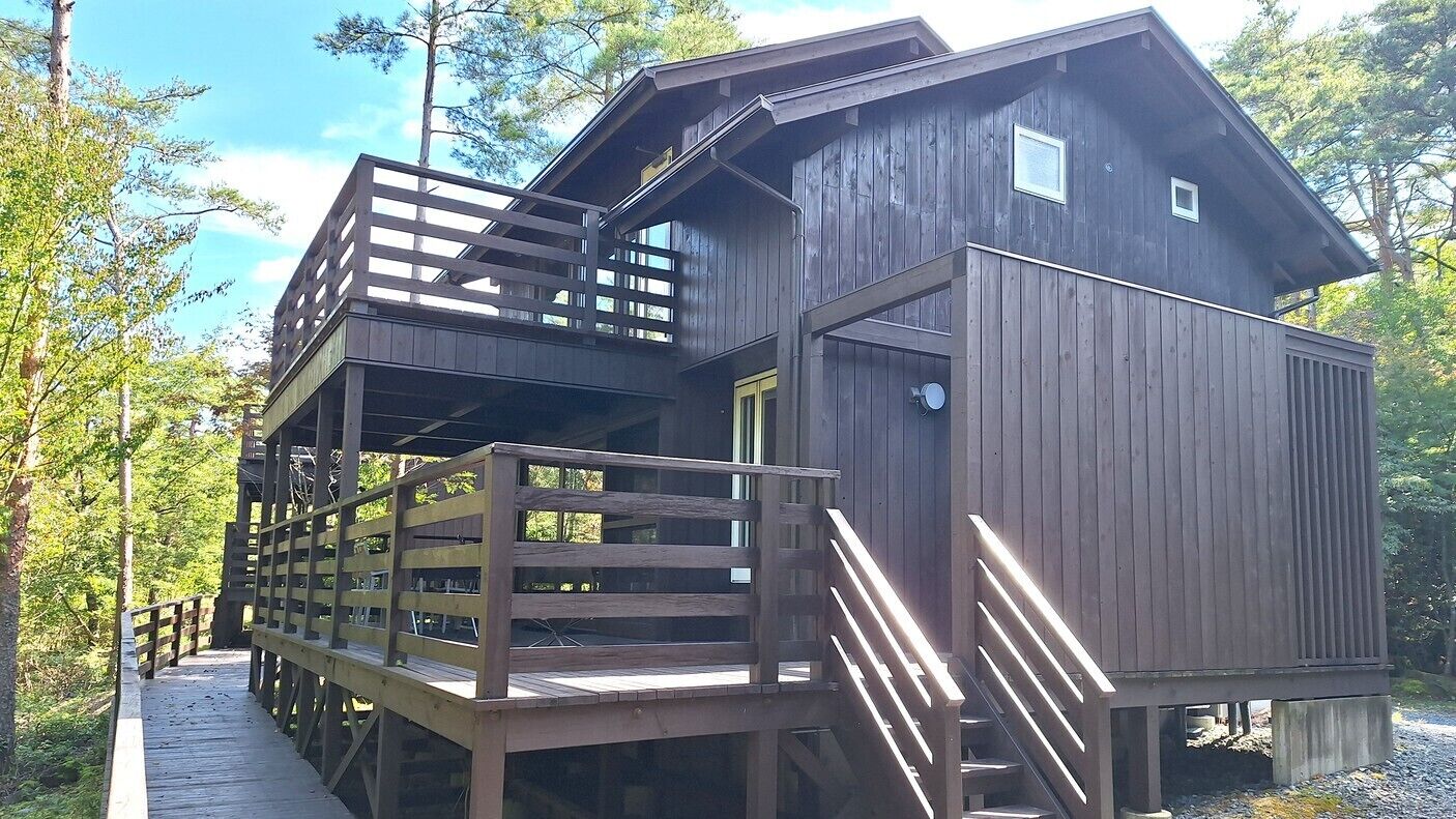 A cabin with a wooden deck, a staircase, and a large window.