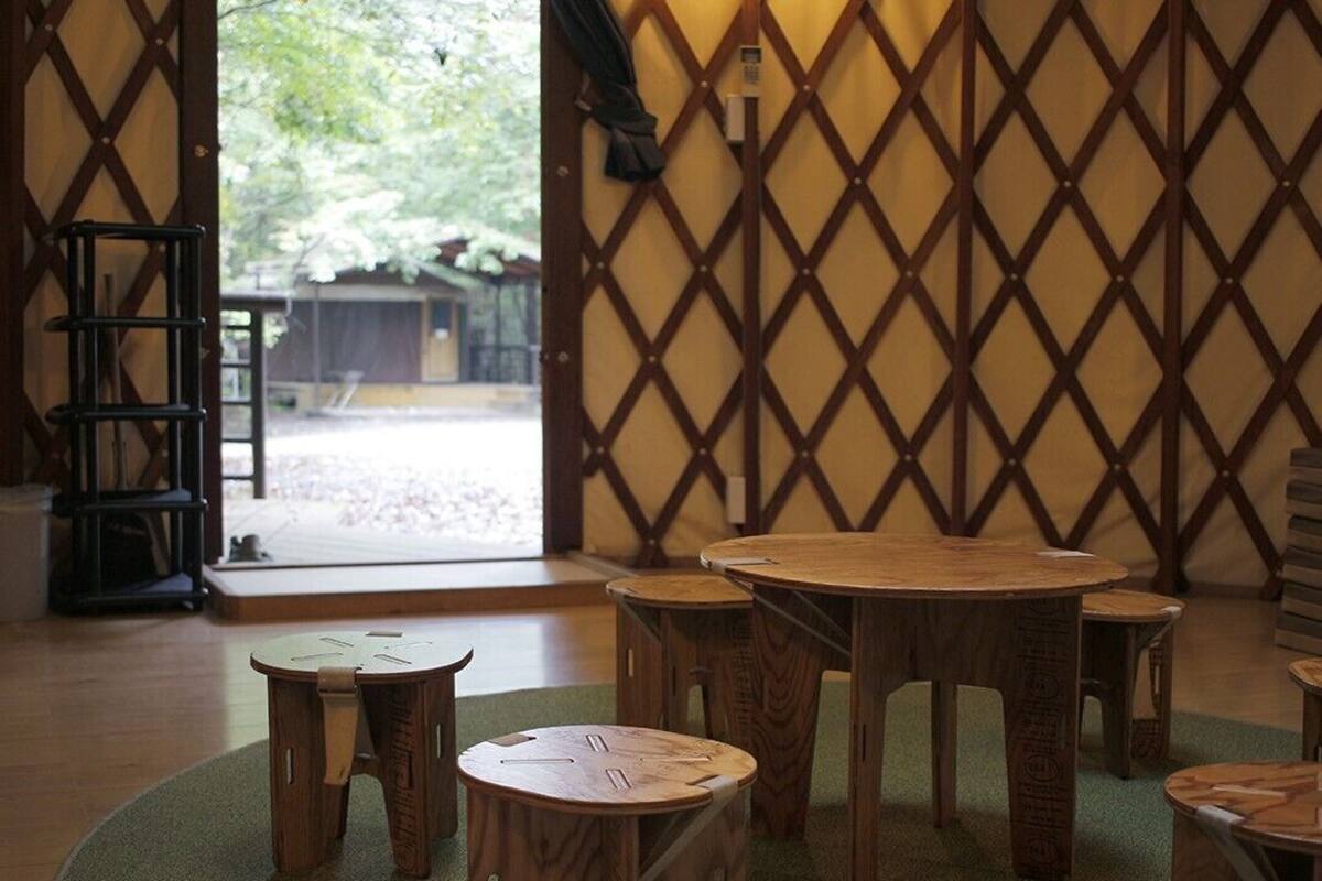 Une pièce avec une cloison en treillis de bois, une table ronde et plusieurs tabourets.
