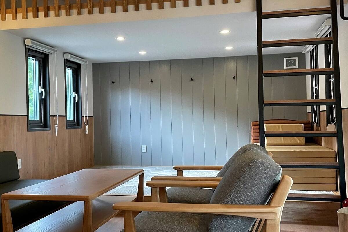 Une pièce comprenant un banc en bois, une table, une chaise, une échelle et un mur avec des panneaux verticaux.