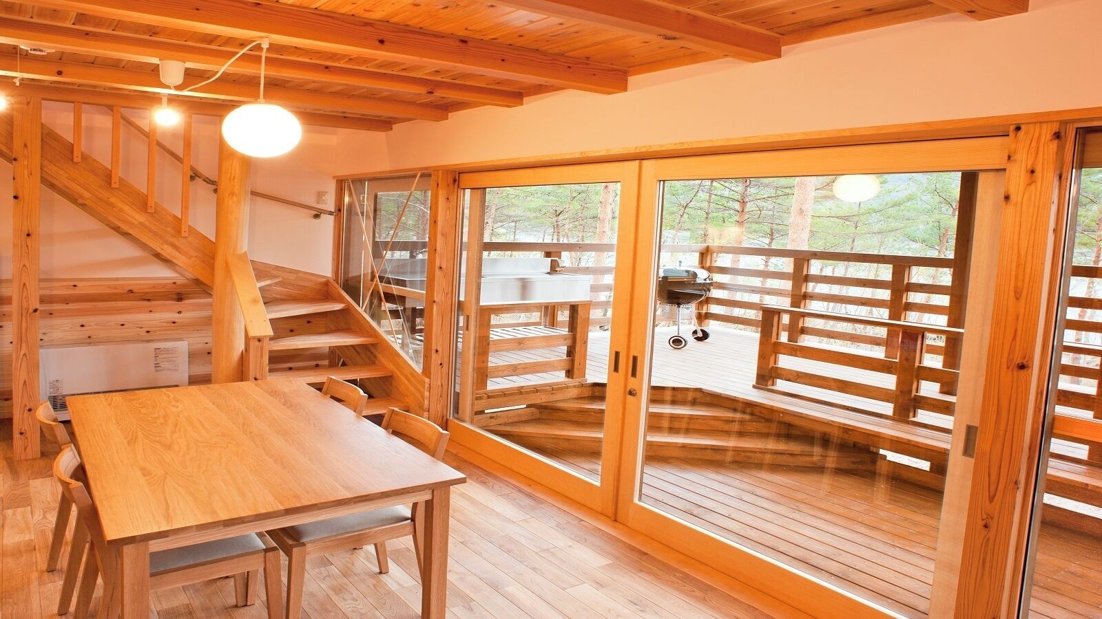 A wooden interior with a staircase, a table, and large sliding glass doors leading to an outdoor deck.
