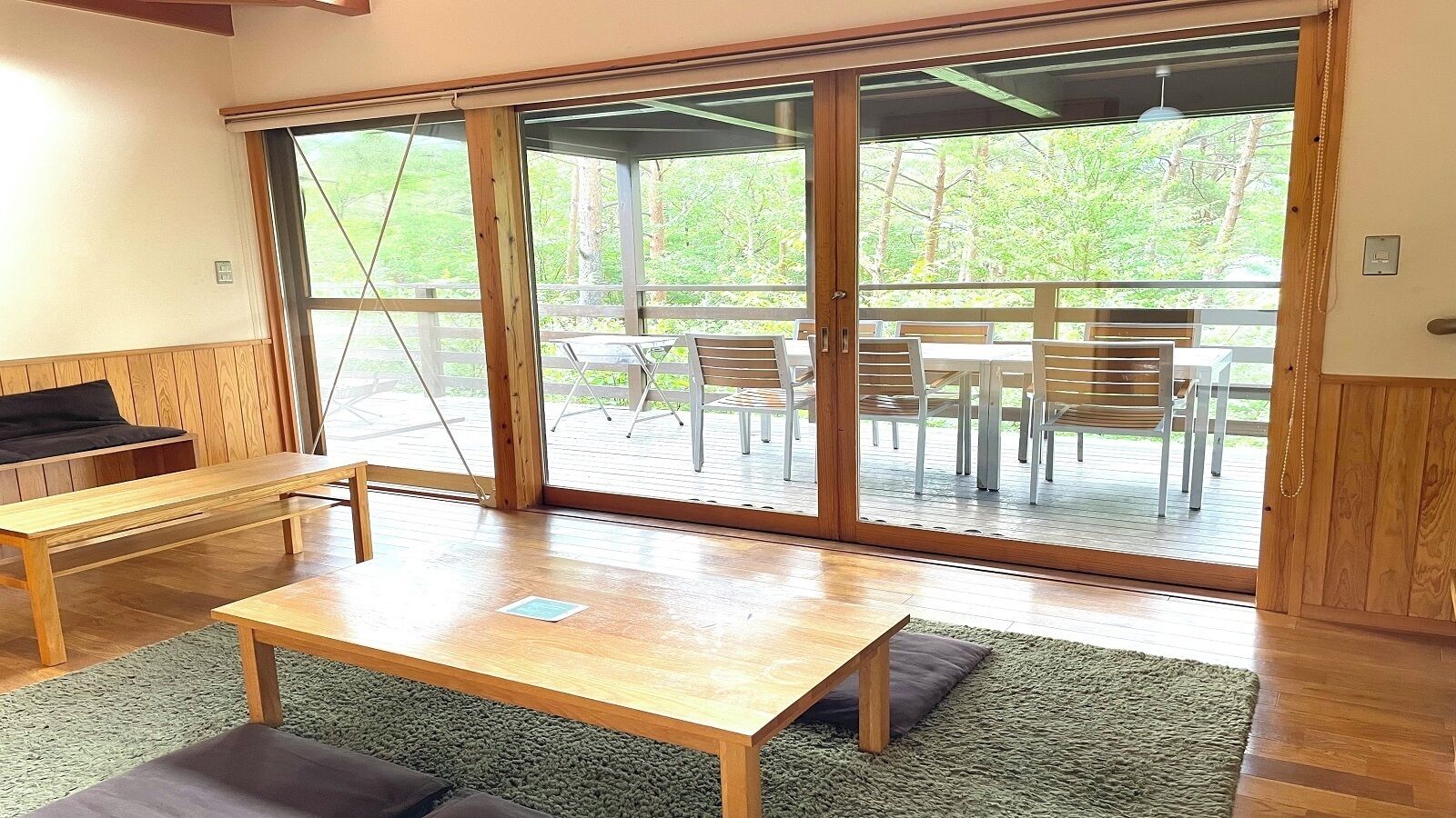 A room with a wooden table, a bench, and a view through large sliding glass doors to an outdoor patio with chairs and a table.