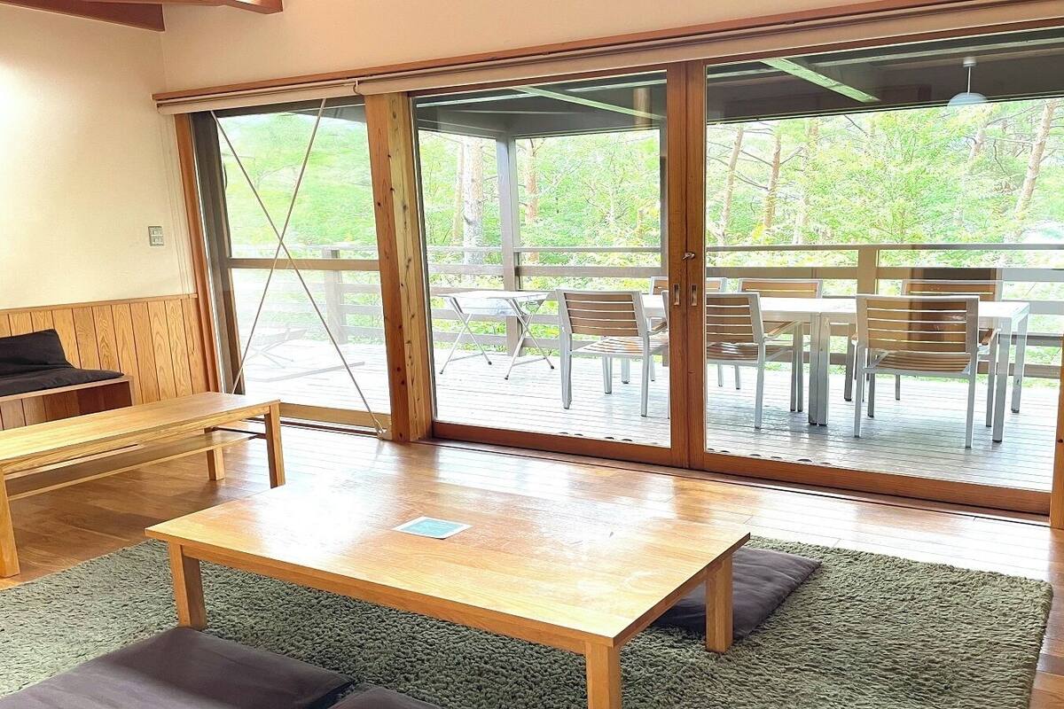 Une pièce avec une table en bois, un banc et une vue sur une terrasse extérieure, accessible par de grandes portes-fenêtres coulissantes, où se trouvent des chaises et une table.
