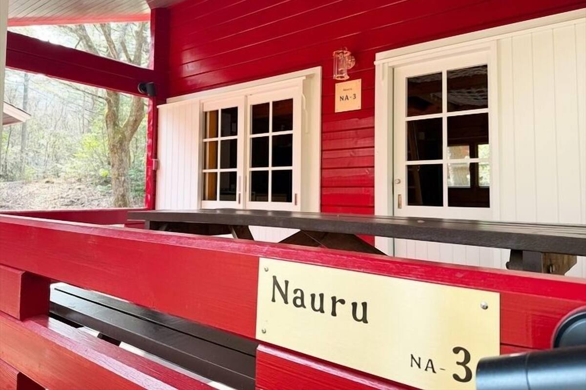 Un bâtiment rouge avec une enseigne indiquant « Nauru NA-3 » et deux fenêtres dotées de volets blancs.