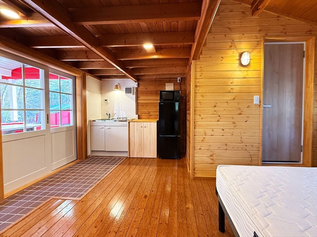 A wooden cabin interior with a kitchen, a bed, and a door.