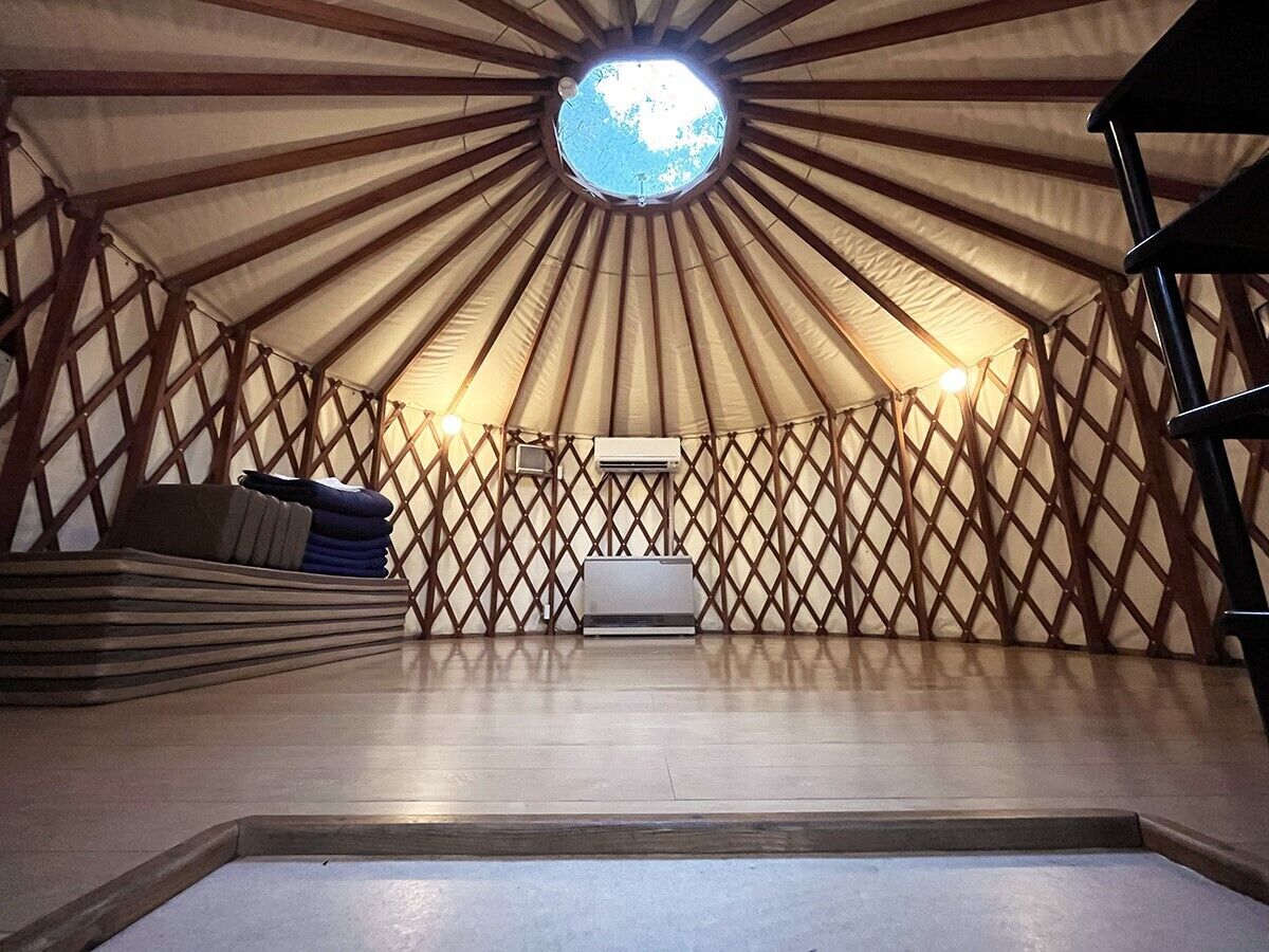 A yurt with a circular skylight, a central bed, and a wooden lattice wall.
