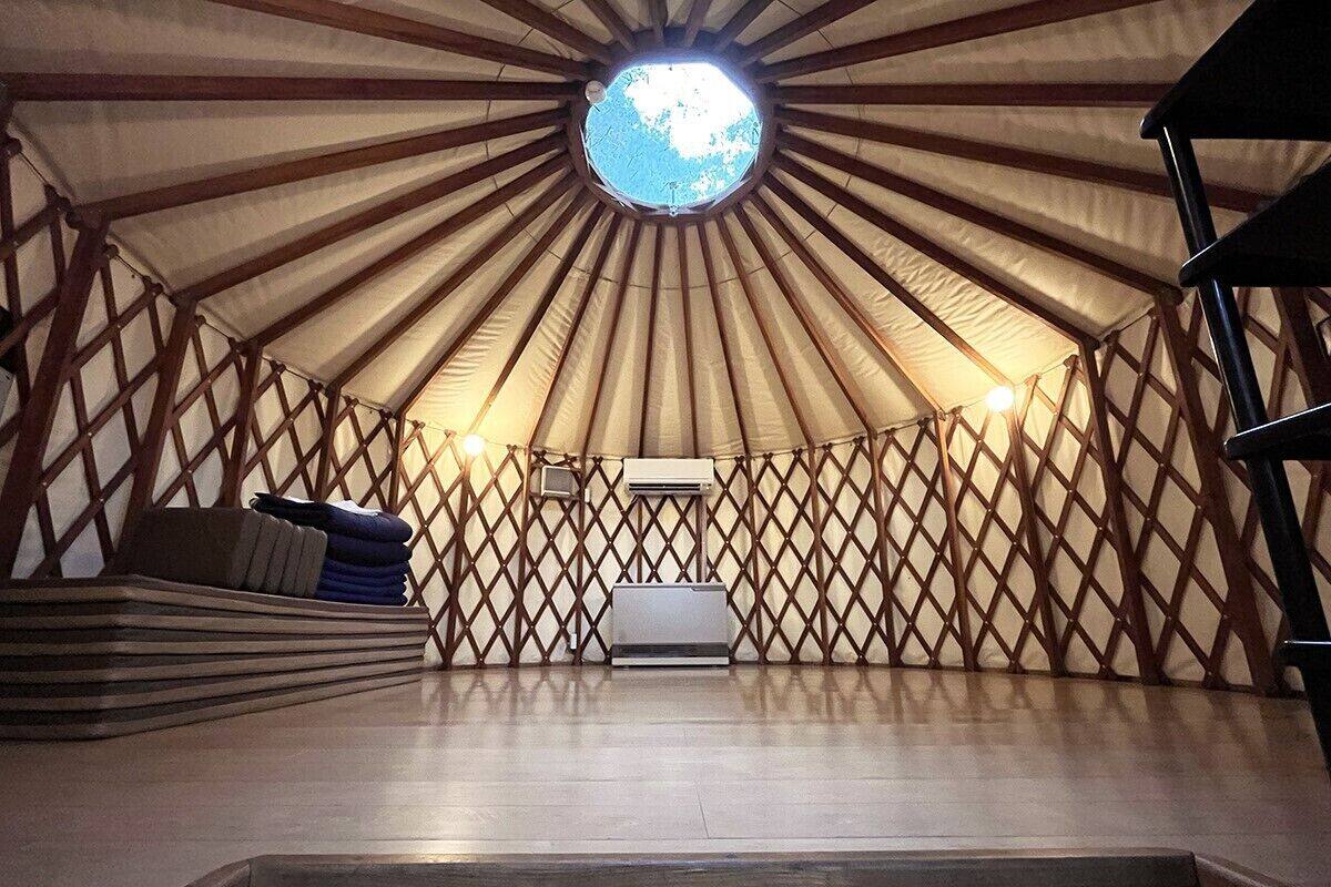 Une yourte dotée d’une lucarne circulaire, d’un lit central et de murs en treillis de bois.