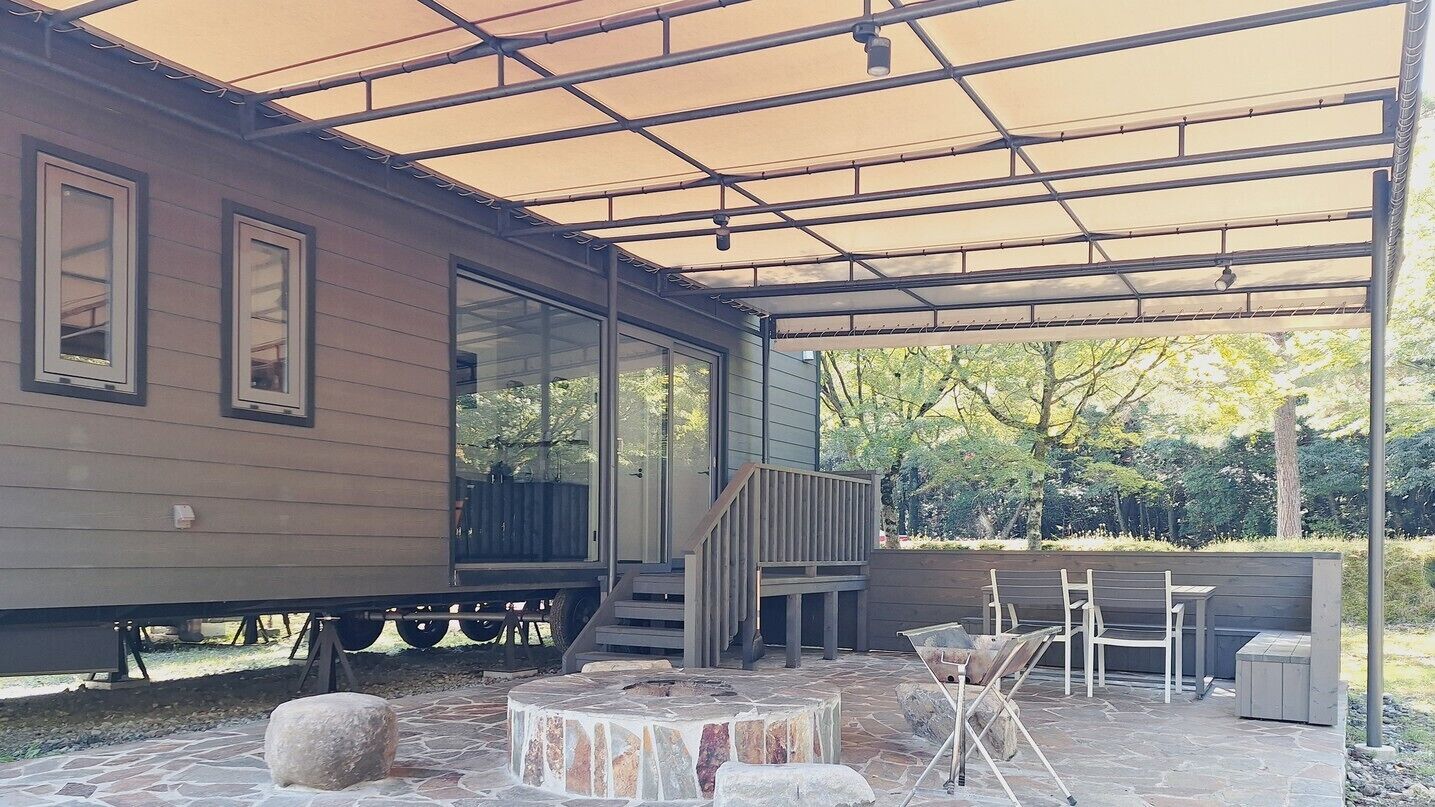 A covered patio with stone flooring, a wooden deck, and outdoor furniture.