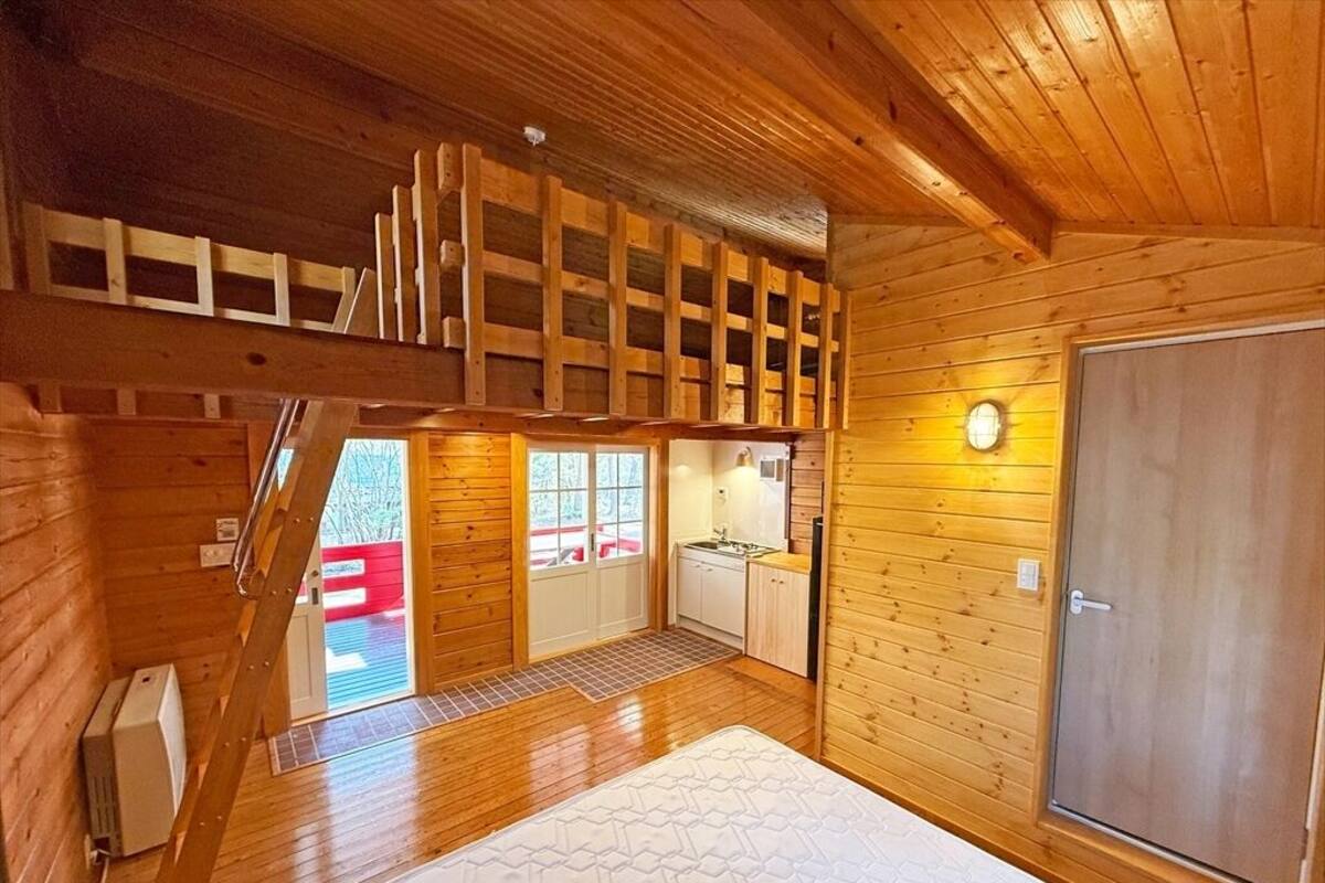 L’intérieur d’une cabane en bois comprend une chambre à coucher située en mezzanine, un coin cuisine et une grande porte.