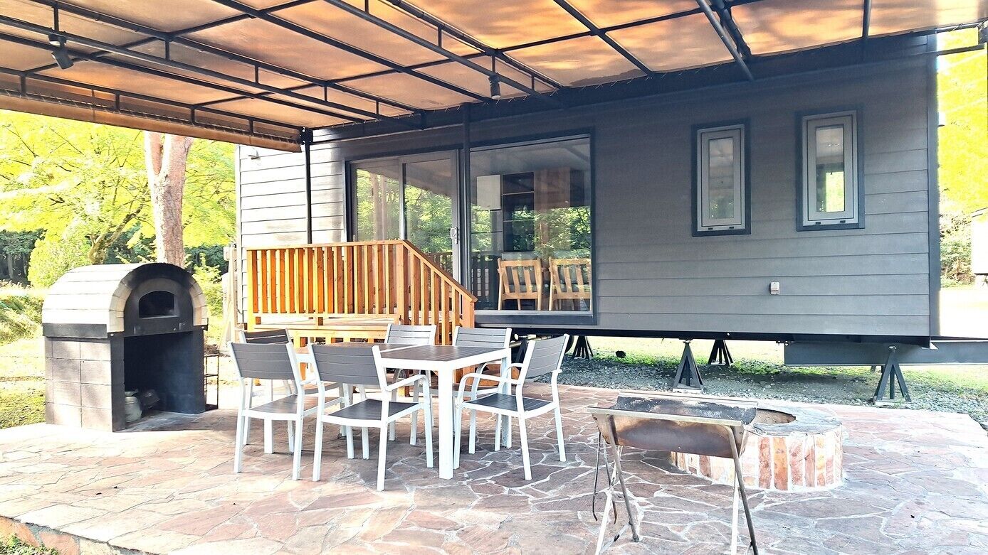 A covered patio with stone flooring, a pizza oven, a grill, and a dining area with chairs and a table.