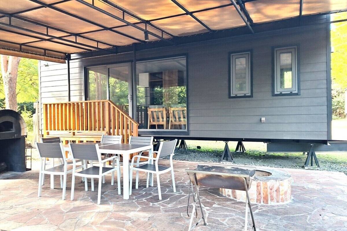Un patio couvert avec un sol en pierre, un four à pizza, un barbecue et un coin repas avec des chaises et une table.
