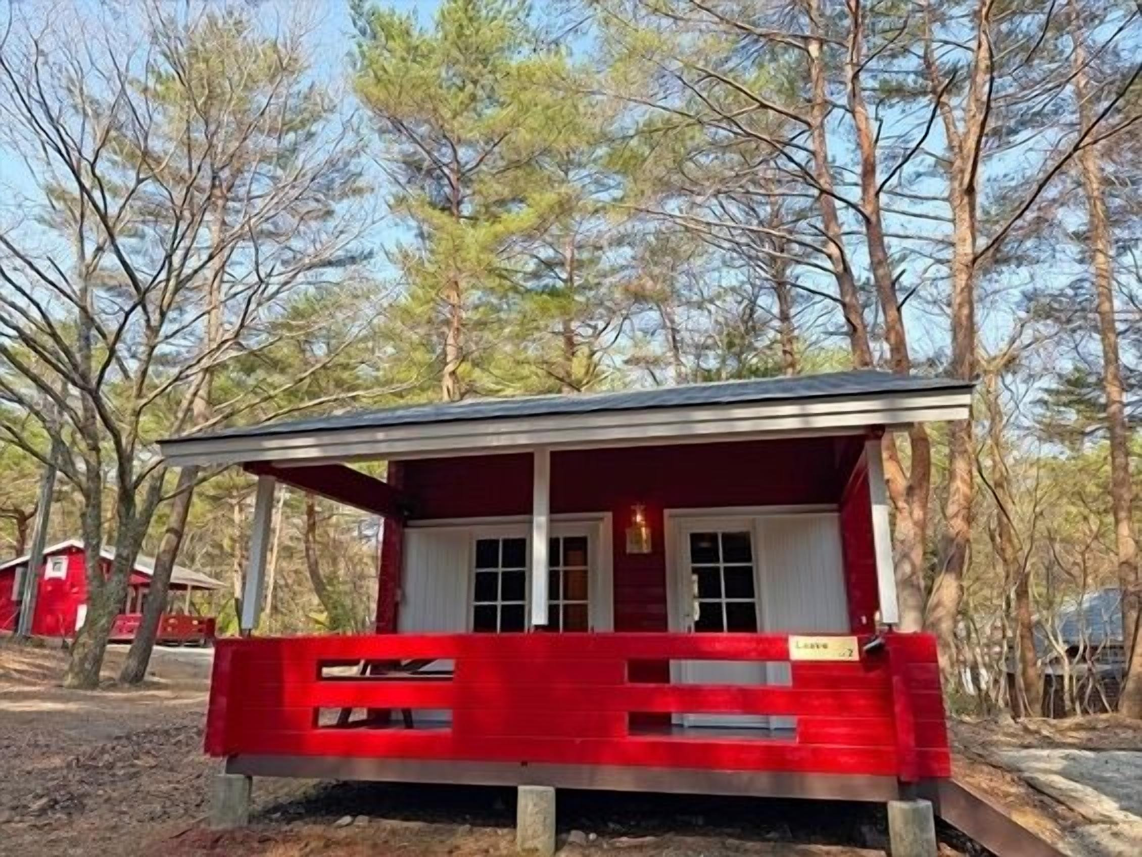 Una piccola baita rossa con un portico, circondata da alberi.