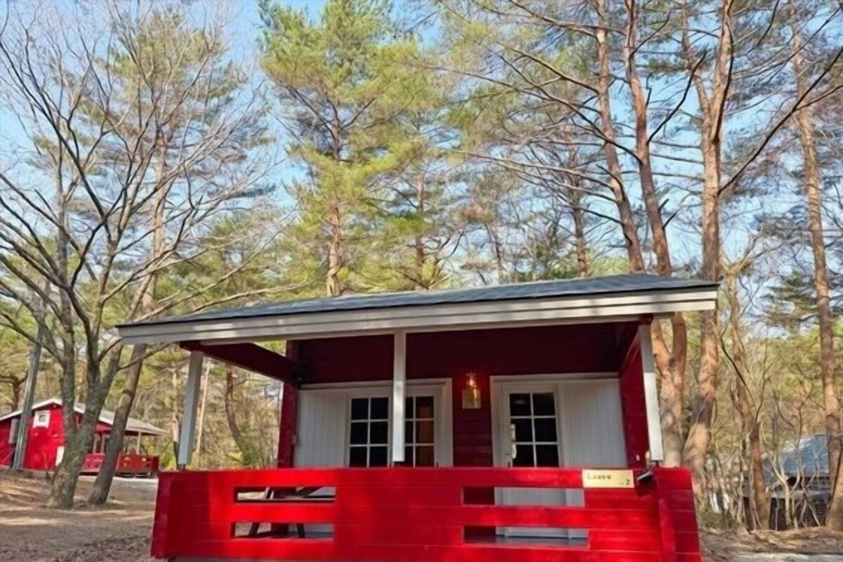 Une petite cabane rouge avec un porche, entourée d’arbres.