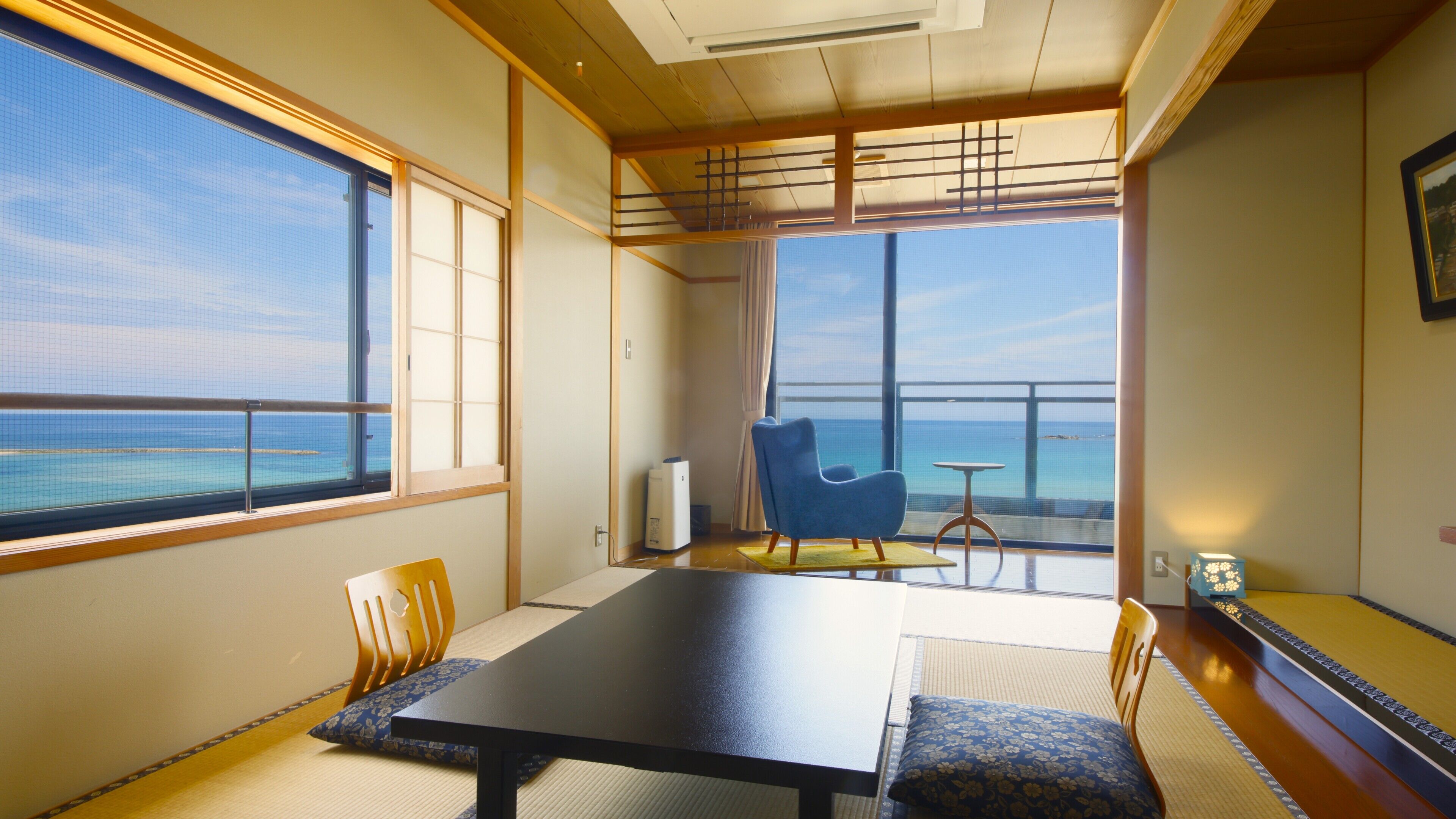 A room with a large table, chairs, a view of the sea, and traditional Japanese decor.