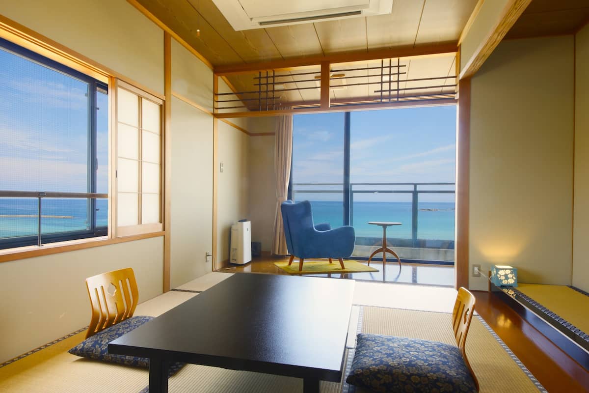 Una stanza con un tavolo grande, sedie, vista sul mare e arredamento in stile tradizionale giapponese.