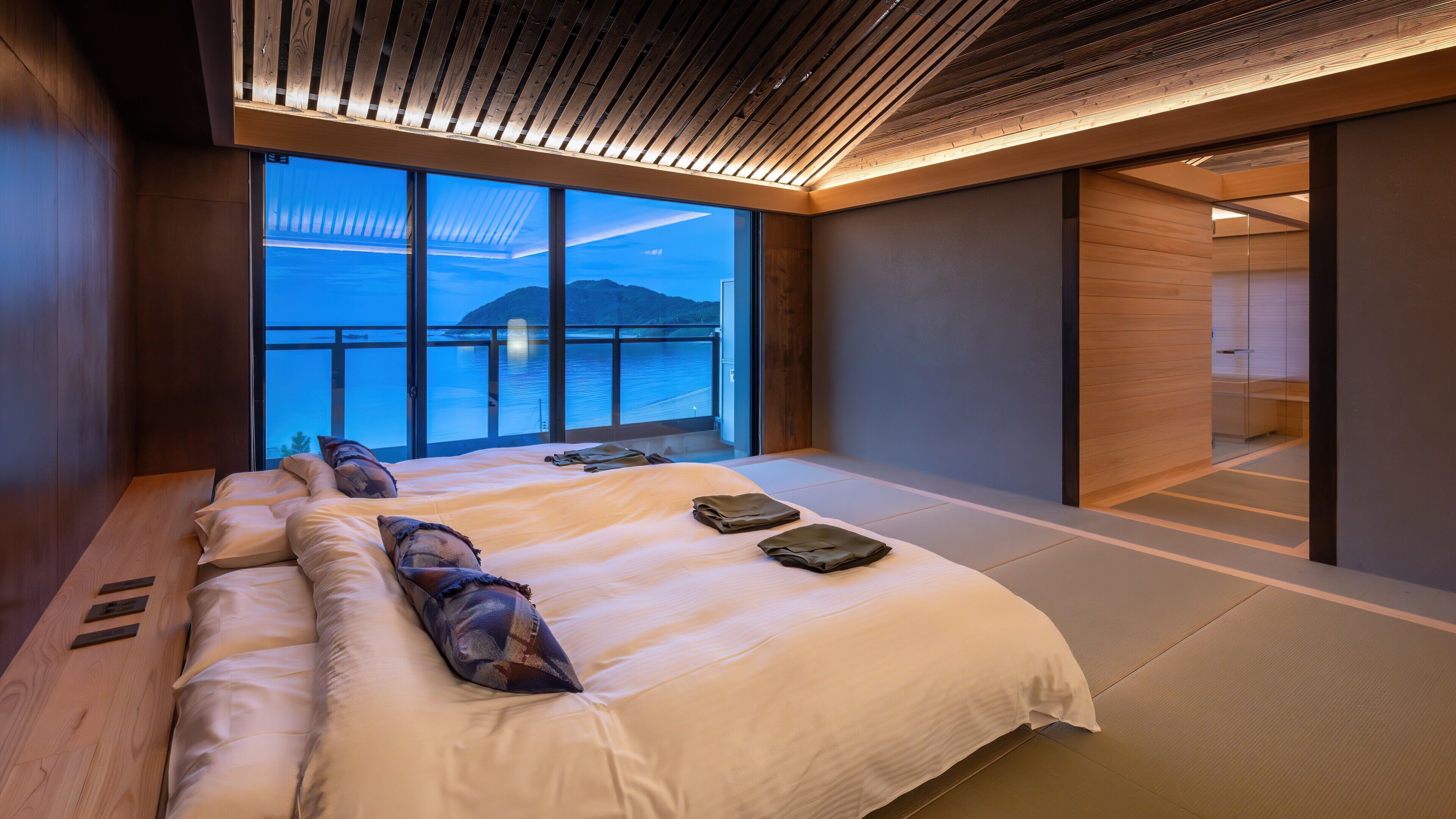 A modern hotel room with a large bed, a view of the sea, and a wooden ceiling.