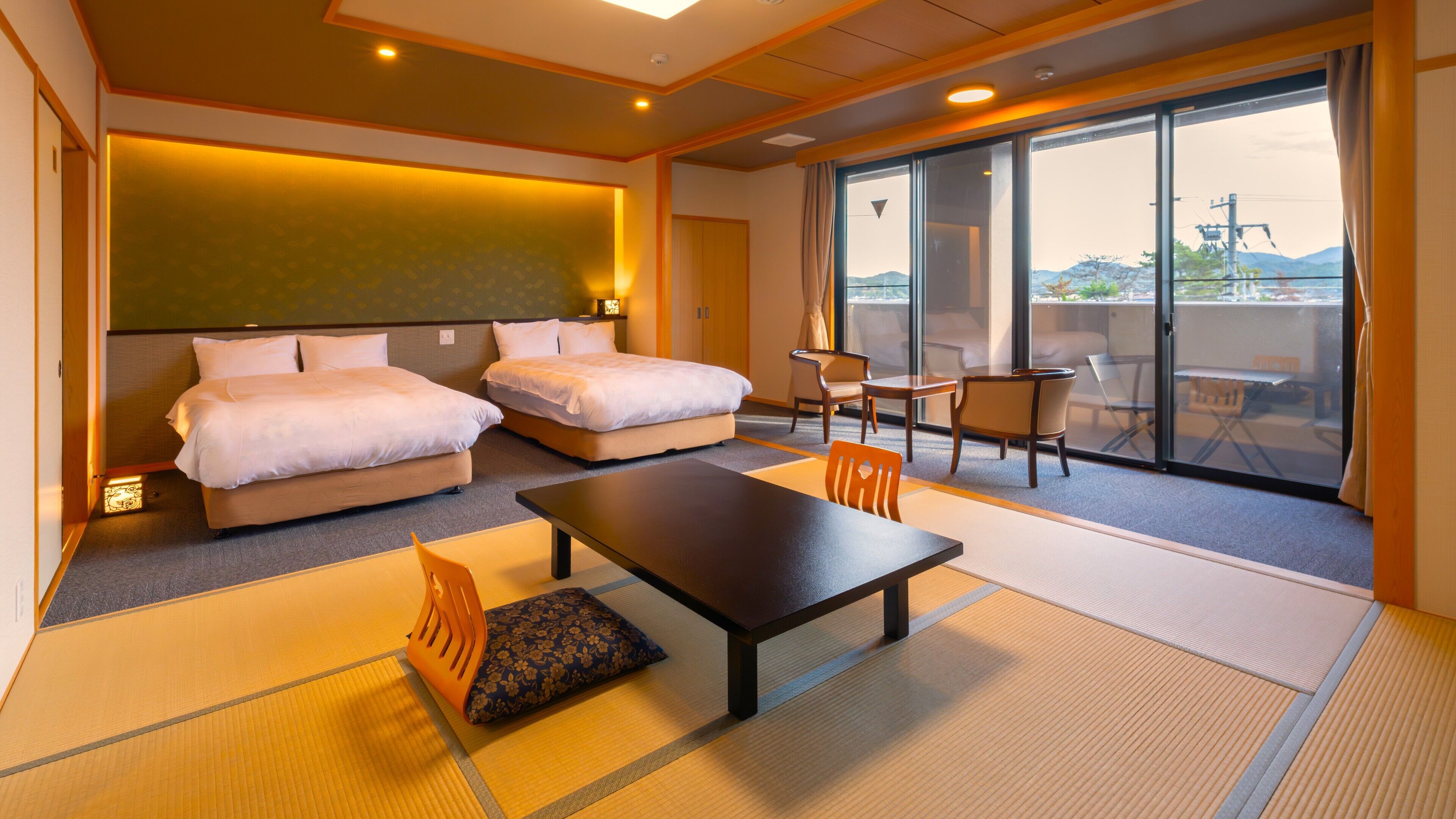 A hotel room with two beds, a dining table, chairs, a sofa, and a view through large windows.