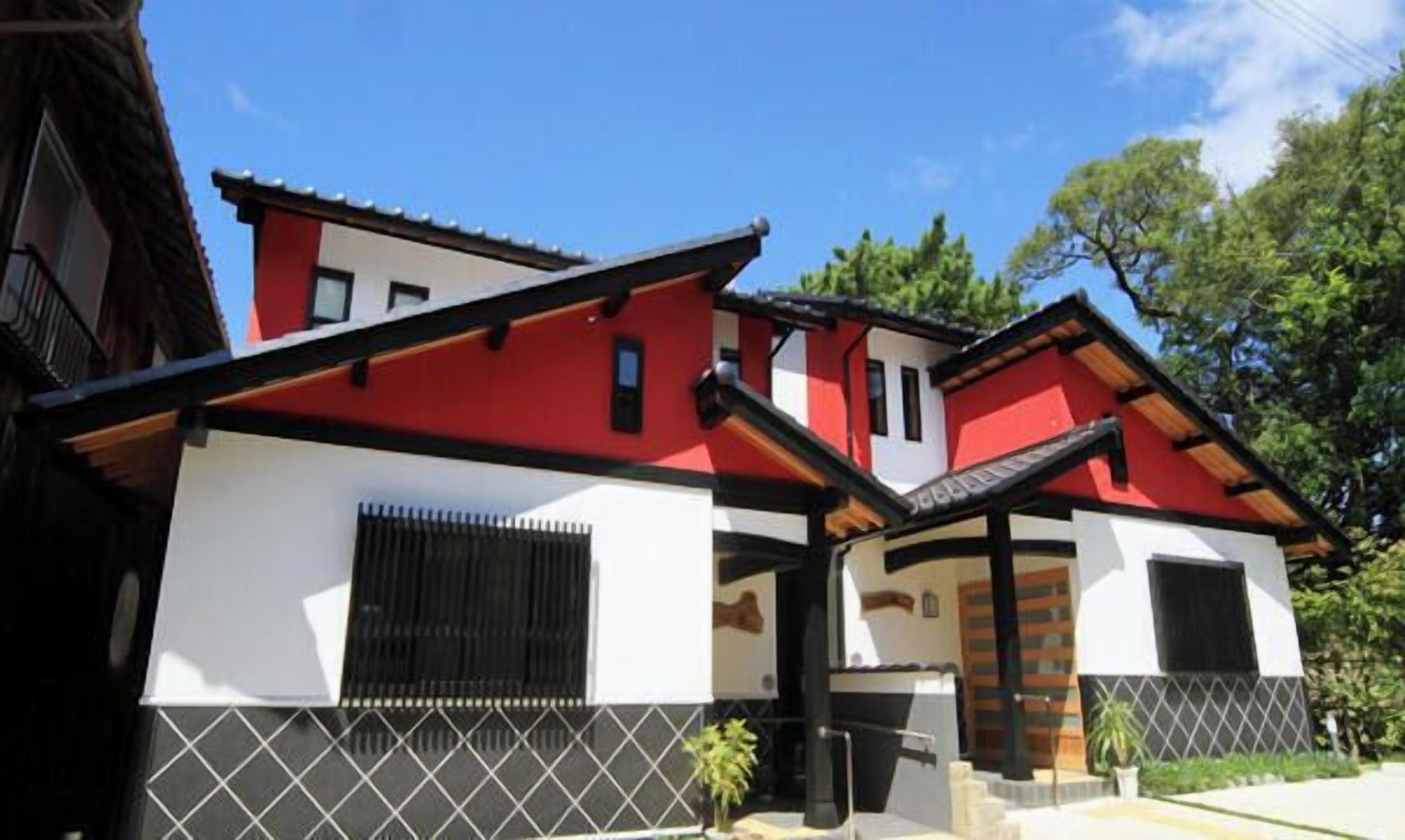 Un bâtiment de style japonais traditionnel, avec une façade rouge et blanche, un toit noir et une entrée carrelée.