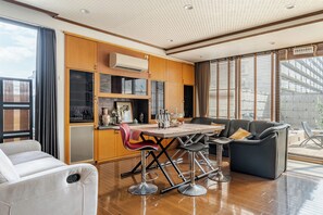 Een moderne keuken met houten kastjes, een zithoek met een tafel en stoelen, en een zangle plek met een bank en fauteuils.