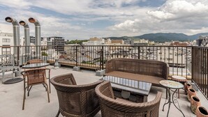 A rooftop terrace with wicker furniture, a glass table, and a view of the cityscape and mountains. - Residence Ferie Nara Station (Nara)