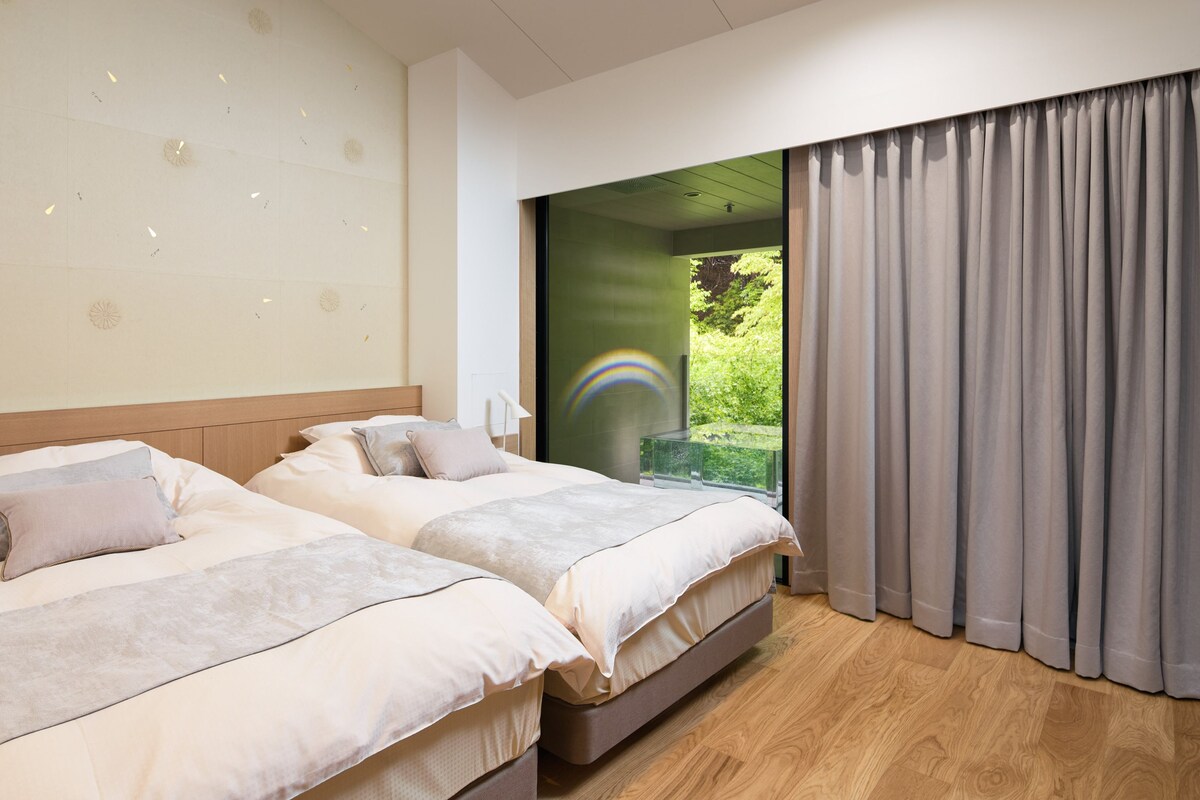 A hotel room with two beds, a large window with a view of greenery, and a ceiling with decorative patterns.