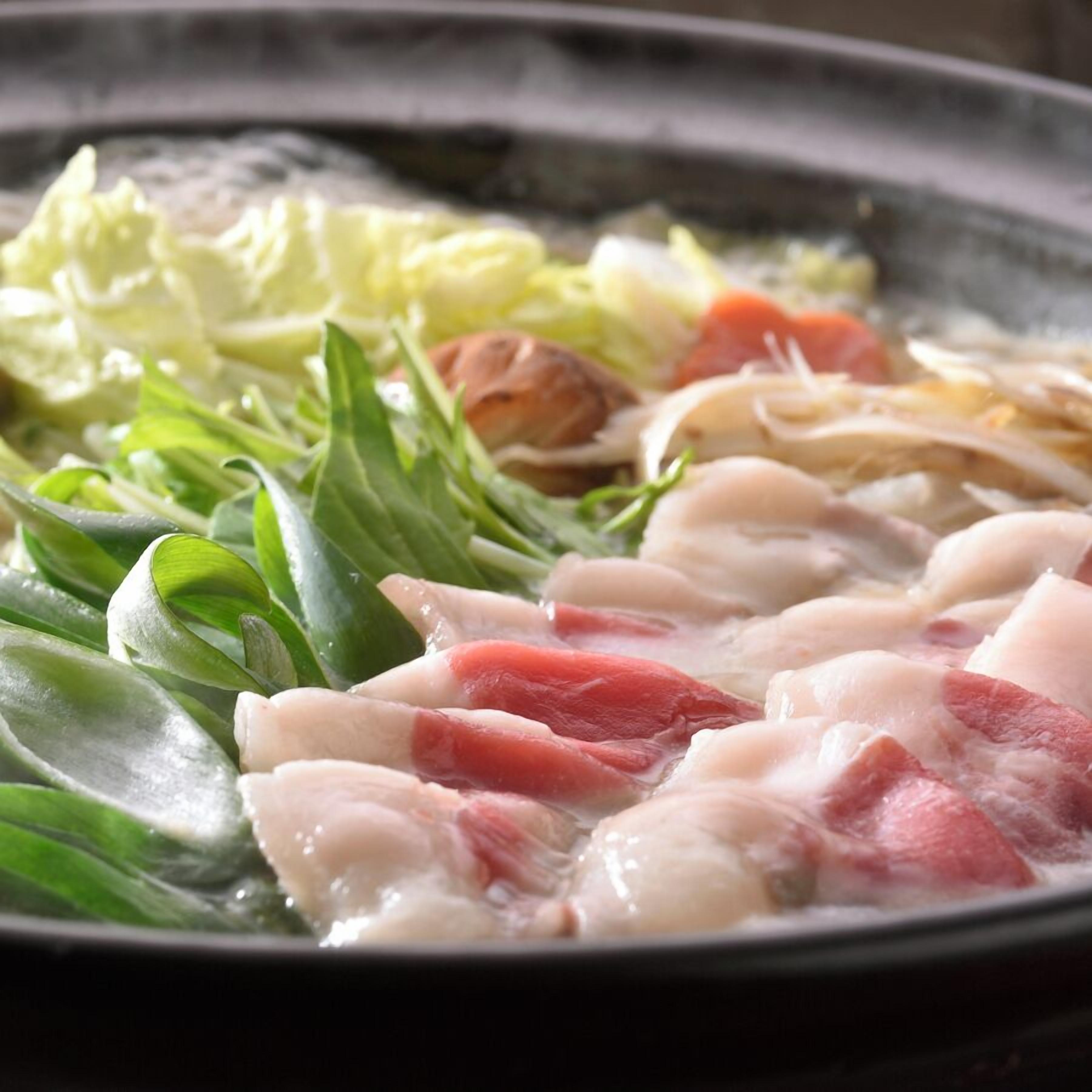 A pan with various ingredients cooking, including leafy greens and chunks of meat.