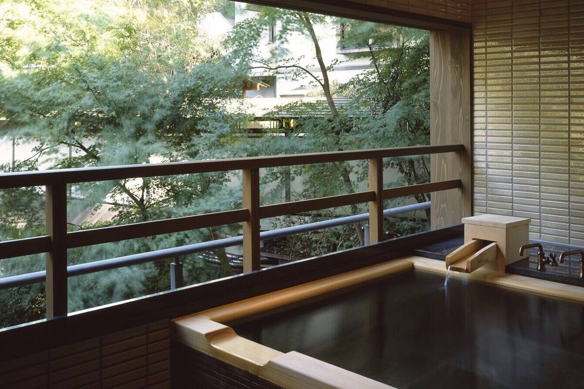 Un jacuzzi con borde de madera, una ventana con vistas a árboles y una barandilla de metal.