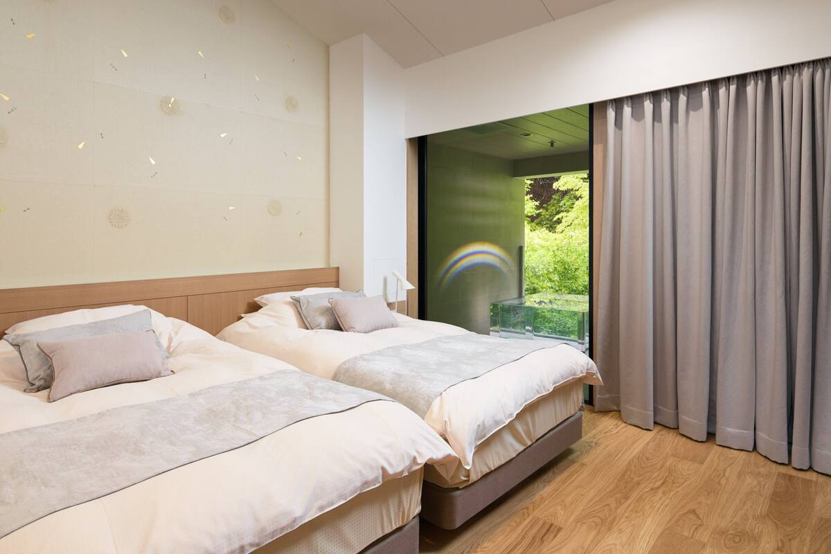 Habitación de hotel con dos camas, un ventanal con vistas a zonas verdes y un techo decorado con motivos ornamentales.