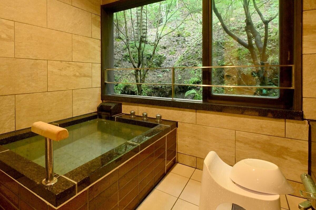 Un baño con bañera, inodoro y ventana con vistas a árboles.