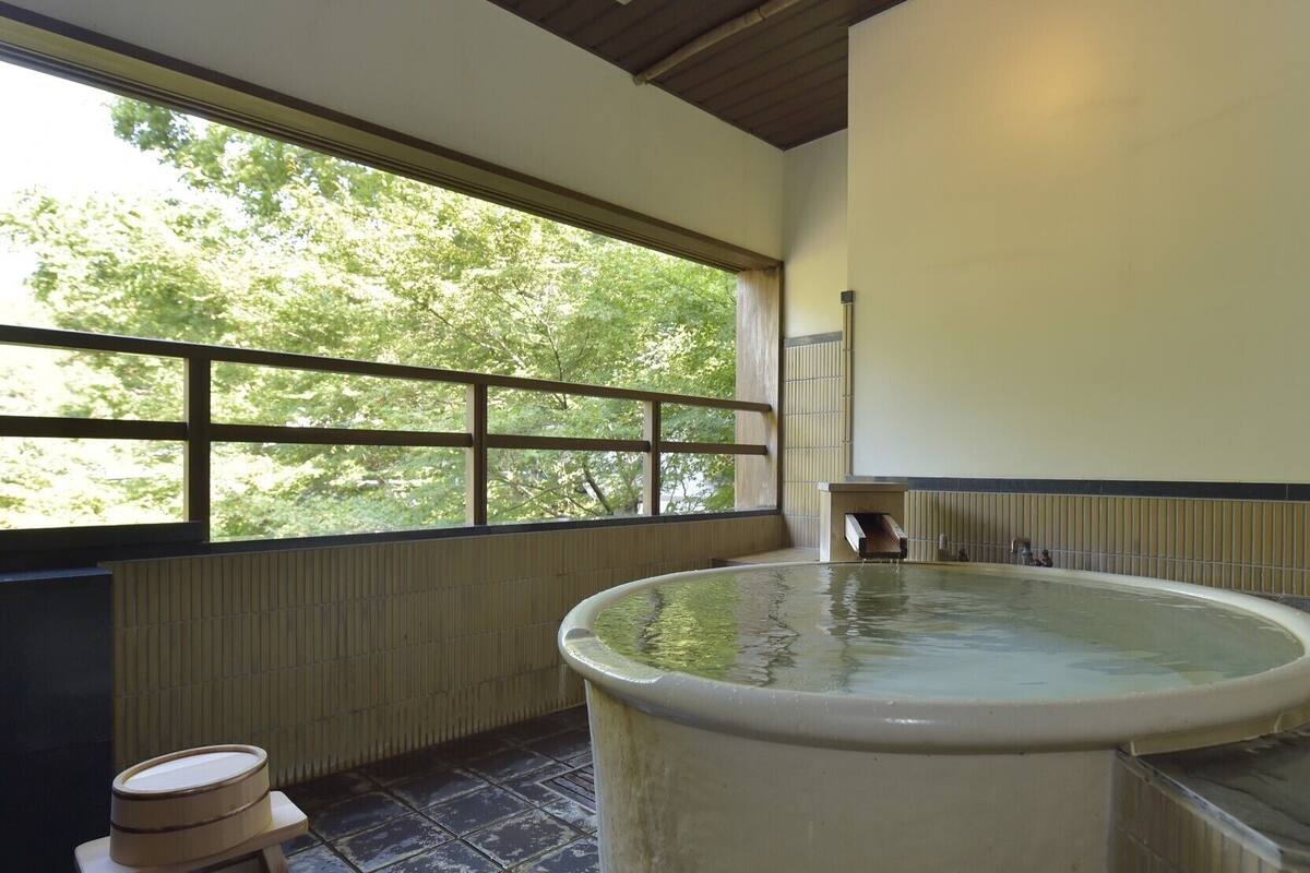 Un jacuzzi en una habitación con un ventanal grande, un banco de madera y suelo de baldosas.